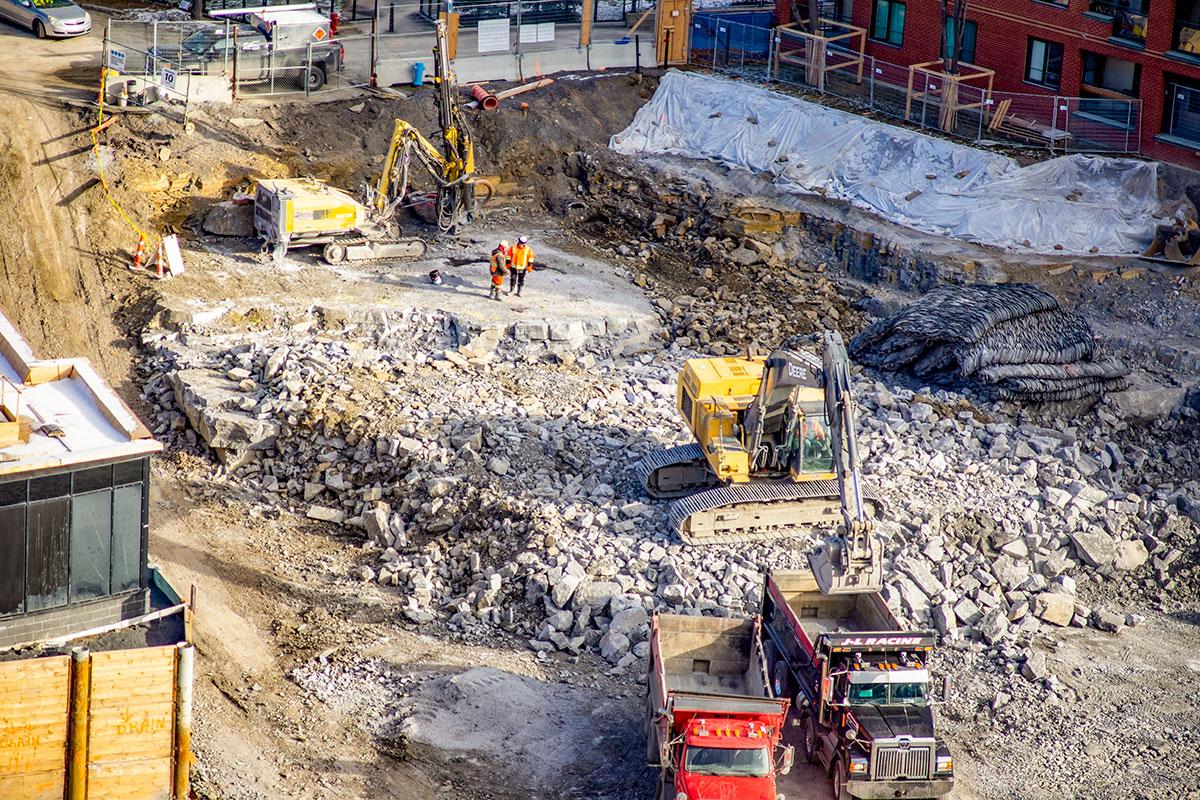 Photo du chantier de l’Îlot Rosemont, à Montréal. Sur cette photo on peut distinguer en haut la foreuse, mais aussi la couche de roche qu'il faut dynamiter, ainsi que les matelas utilisés comme pare chocs sur la zone dynamitée - Crédit photo Laurent Canigiani